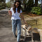 Woman walking a dog on a street with trees and greenery in the background