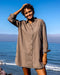 Woman wearing a beige shirt dress standing on a beach with blue sky and ocean in the background
