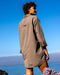 Person wearing a beige jacket standing against a blue sky and ocean backdrop
