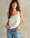 A woman wearing a white tank top and blue jeans.