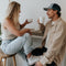 Two people sitting indoors, holding coffee cups and engaged in conversation.