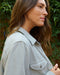 Woman wearing a light gray jacket outdoors with greenery in the background